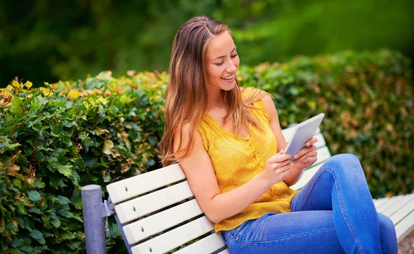 Technologie houdt haar op de hoogte waar ze ook is. Foto van een jonge vrouw met een digitale tablet op een bankje in het park. — Stockfoto