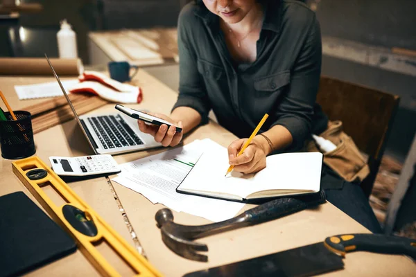 Prestando total atenção aos detalhes. Foto recortada de uma atraente jovem carpinteiro trabalhando em seu laptop na oficina. — Fotografia de Stock