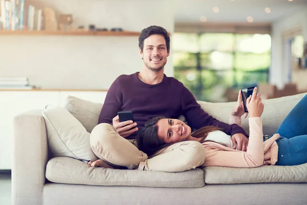 Compartimos nuestras vidas y nuestra radio. Retrato de una joven pareja sonriente usando tabletas digitales mientras se relajan juntos en el sofá en casa. — Foto de Stock