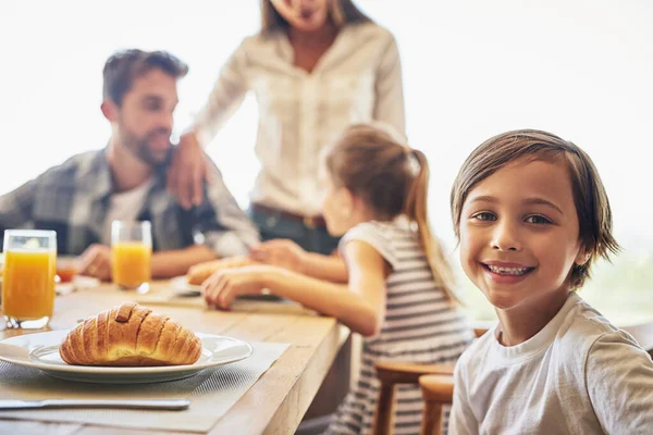 We vullen onze buikjes voor de komende dag. Portret van een kleine jongen ontbijten met zijn familie op de achtergrond. — Stockfoto