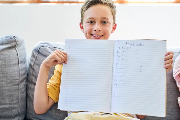 Blij met zijn voltooide huiswerk. Gehakt schot van een kleine jongen die een notitieboekje met zijn huiswerk in het op de bank thuis. — Stockfoto