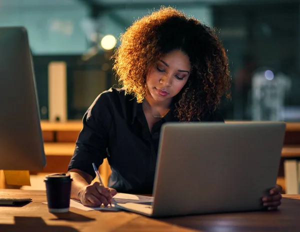 Essere i migliori richiede duro lavoro e dedizione. Girato di una giovane donna d'affari che usa un computer portatile e scrive appunti durante una tarda notte al lavoro. — Foto Stock