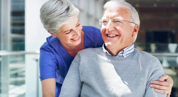 Always laugh when you can, its free medicine. Cropped shot of a happy senior man sitting in a wheelchair while his attractive mature nurse aid assists him indoors. — Stock Photo, Image