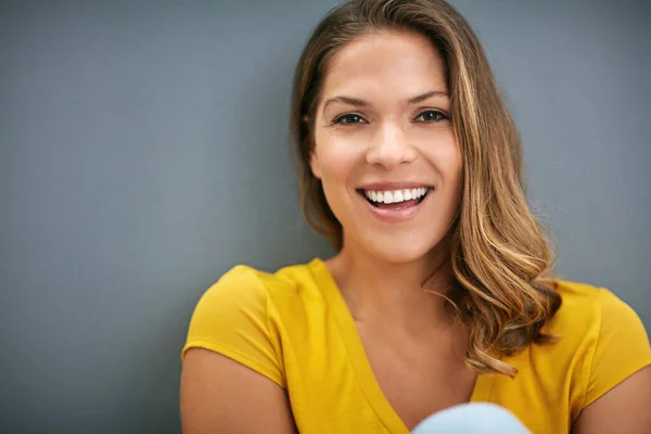 彼女は笑わずにはいられない。灰色の壁にポーズをとる若い女性のショット. — ストック写真