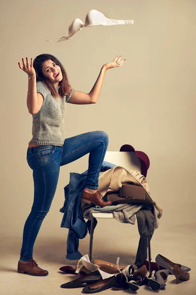 Αυτό είναι. Θα μείνω με τζιν και πουκάμισο. Στούντιο πλάνο μιας νεαρής γυναίκας που διαλέγει ρούχα στοιβαγμένα σε μια καρέκλα πάνω σε καφέ φόντο. — Φωτογραφία Αρχείου