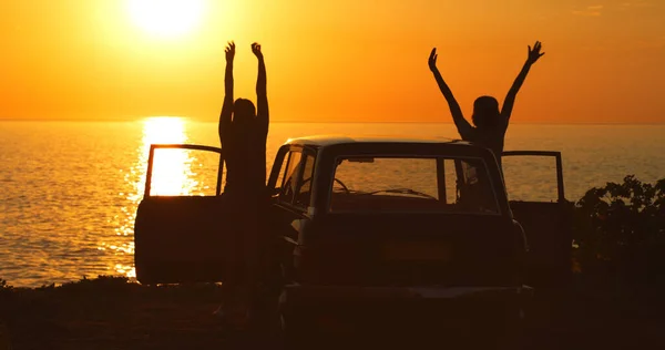 De zee brengt hun kleine meisjes naar buiten. Achteraanzicht van twee onherkenbare vriendinnen die juichen met opgeheven armen tijdens een roadtrip op het strand. — Stockfoto