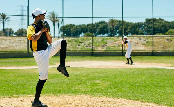 Dává své nadhazovací schopnosti do práce. Full length shot of a handsome young baseball player pitching a ball during a match on the field. — Stock fotografie
