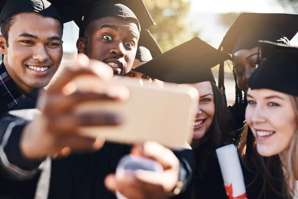 Los fuegos artificiales comienzan hoy. Fotografía de un grupo de estudiantes tomando selfies con un teléfono móvil el día de la graduación. —  Fotos de Stock
