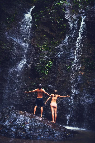 Chłodzenie, styl dżungli. Zdjęcie z tyłu młodej pary stojącej pod wodospadem w dżungli. — Zdjęcie stockowe