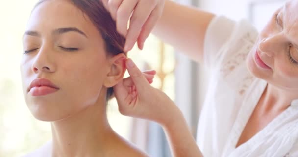 若い混合人種の女性が鍼治療の針を耳に差し込む 温泉で顔面鍼治療を楽しむ混合レース女 鍼治療中の成熟した全体的なヒーラーの話 — ストック動画