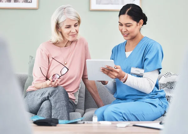 Shot of a female nurse using a digital tablet while sitting with her patient