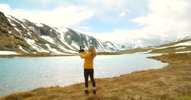 4Kビデオ映像の認識できない女性が立って 彼女の携帯電話を使用して湖を撮影するMore Romsdal — ストック動画