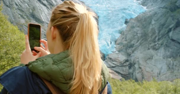 若い女性が立っていると彼女の携帯電話を使用して写真を撮る Briksdal Glacier — ストック動画