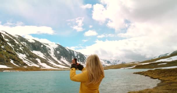 在Mre Romsdal 一名年轻妇女站在那里用手机拍摄湖面的4K视频 — 图库视频影像
