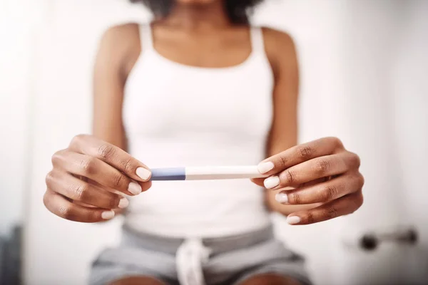 Shot of an unrecognizable woman holding a pregnancy test stick while sitting on the toilet.