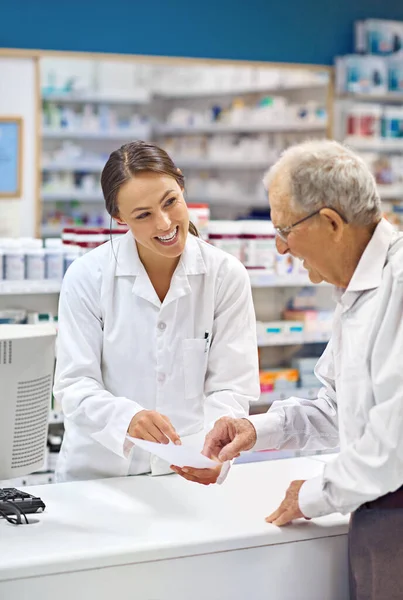 Shot of a young pharmacist helping an elderly customer at the prescription counter.