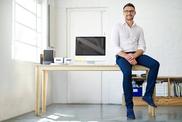 Full length portrait of a businessman sitting a desk in his office.