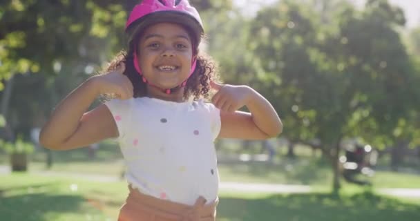 在公园里一个阳光灿烂的日子里 一个戴着粉色头盔跳舞和竖起大拇指的快乐而兴奋的小女孩 可爱的孩子是积极的 并支持保护装备 同时有乐趣 — 图库视频影像