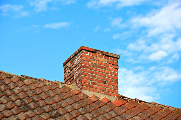 Red brick chimney designed on slate roof of a house building outside with cloudy blue sky background and copyspace. Construction of exterior escape chute built on rooftop for fireplace smoke and heat.