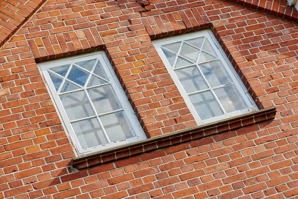 Old stone wall with two rectangular windows. Close up of rectangular windows of a building with a red brick wall. Patterned windows on a red stained brick wall of an old building or house.