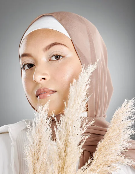 灰色の背景にパンパス小麦の植物とポーズ茶色のスカーフを身に着けている1つの美しい若いイスラム教徒の女性のスタジオの肖像画 伝統的なヒジャーブで覆われた顔の化粧を身に着けている最も控えめなアラブ — ストック写真