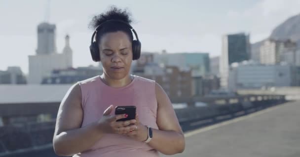 プラスサイズの女性は ヘッドフォンで音楽を聞いて 行使し 市内の減量を追跡するために携帯電話を使用しています ぽっちゃりアクティブLatino女性取得フィットとともに日常屋外ワークアウトで町 — ストック動画