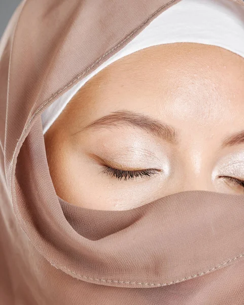 Modest arab woman wearing makeup with face covered in a brown traditional hijab. Closeup of one beautiful young muslim female with radiant skin and eyes closed wearing a religious headscarf covering.