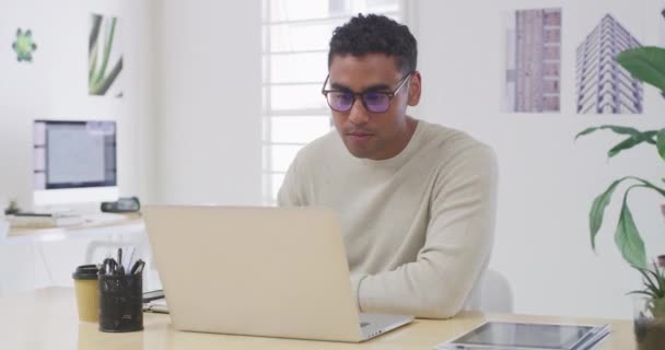 オフィスのノートパソコンで仕事をしながらアイデアを考えるビジネスマンに焦点を当てました スタートアップの代理店でコンピュータ上で計画しながら インスピレーションのためにインターネットを閲覧メガネを持つ若いデザイナー — ストック動画