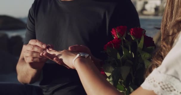 ビーチでの提案の後 ロマンチックなカップルが婚約します 彼は彼女の指にダイヤモンドリングを置くように若い女性は彼女の婚約者への愛情を示す赤いバラの束を保持します — ストック動画