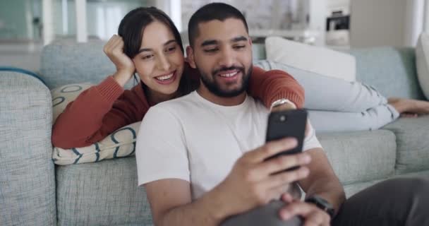 電話を使用してテキストメッセージ オンラインチャット またはソーシャルメディアを閲覧する幸せと愛情のあるカップル 恋の彼氏と彼女が一緒にソファで笑ってリラックスします 自宅で夫と妻 — ストック動画