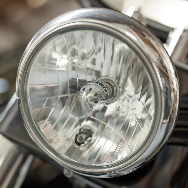 Closeup of a round headlight on a classic motorbike. One light bulb on a well maintained sliver chrome coated retro motorcycle. Motor vehicle accessories and parts. Glass lamp light with silver fram.