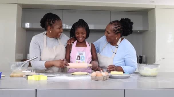 いくつかの生地を圧延しながら 自宅で母親と祖母と一緒に焼く幸せな小さなアフリカ系アメリカ人の女の子 女性家族の絆と女の子を教える方法を焼くと台所で調理 — ストック動画