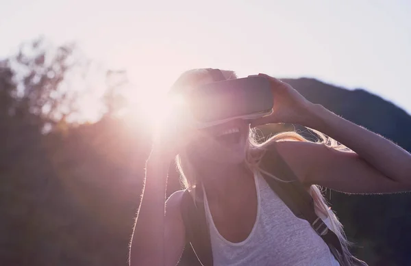 Excited young woman on holiday using VR headset. Young woman on holiday excited about using VR headset. Young happy woman using VR headset during hike on holiday.