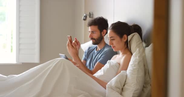 Серйозна Молода Пара Розслабляється Ліжку Використовуючи Мобільні Телефони Разом — стокове відео