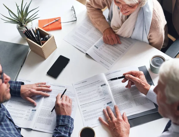 A mature couple meeting with a financial advisor to discuss retirement plans from above. A senior couple meeting a banker to sign contracts together. A mature couple reading and signing documents.