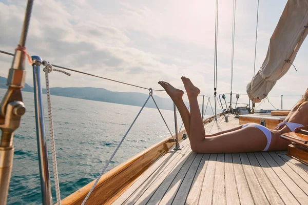 Legs of sexy woman in white bikini lying on boat sunbathing. Woman in white bikini tanning legs on a boat. Sexy legs of woman wearing white bikini sunbathing on a cruise.