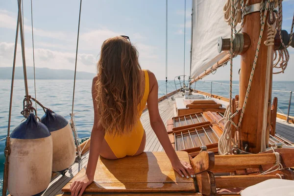 Woman in yellow swimwear looking at the ocean view sitting on a boat. Woman in yellow swimwear sitting on boat looking at the view. Woman enjoying the ocean view from a boat on a cruise.