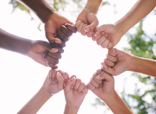 Closeup of fists in a circle outside in nature. Diverse group of peoples fists touching. Multiethnic people with their fists together.