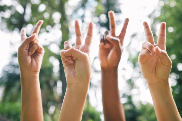 Hands showing the peace sign in the air outside. Diverse group of people gathering for world peace. Closeup of multicultural peoples hands showing the peace sign.