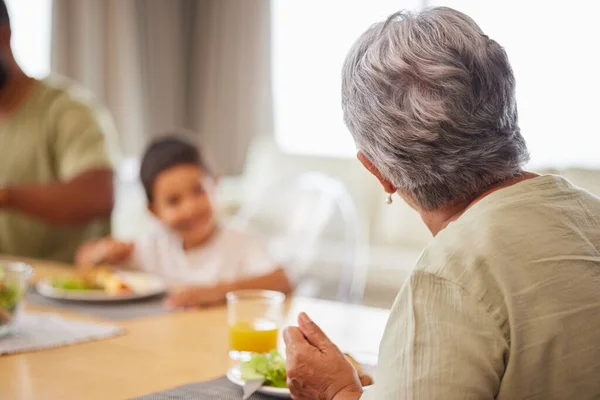 Rear view closeup of a mature mixed race woman having lunch with her family at the table in the lounge at home.