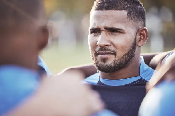 Closeup mixed race rugby player standing in a huddle with his teammates outside on a field. Hispanic male athlete looking serious and focused while huddled together with his team. Ready for the game.
