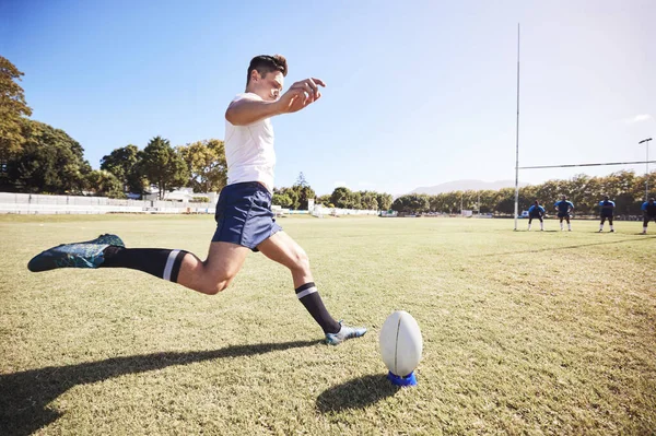 One caucasian rugby player kicking off during a rugby match outside on the field. Young athletic man taking a penalty or attempting to score a conversion during a game. Hes the kicker on the team.