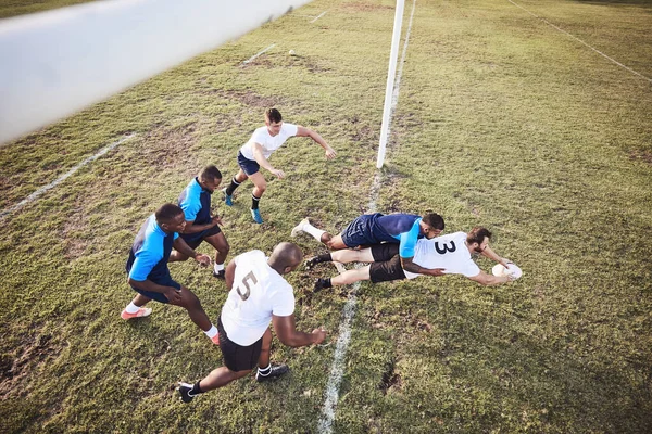 Above caucasian rugby player diving to score a try during a rugby match outside on a field. Male athlete making a dive to try and win the game for his team. Young man reaching out for the try line.