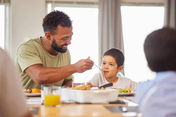 Closeup of a mixed race male and his son enjoying some food at the a table during lunch at home in the lounge. Hispanic father smiling and eating alongside his son at home.
