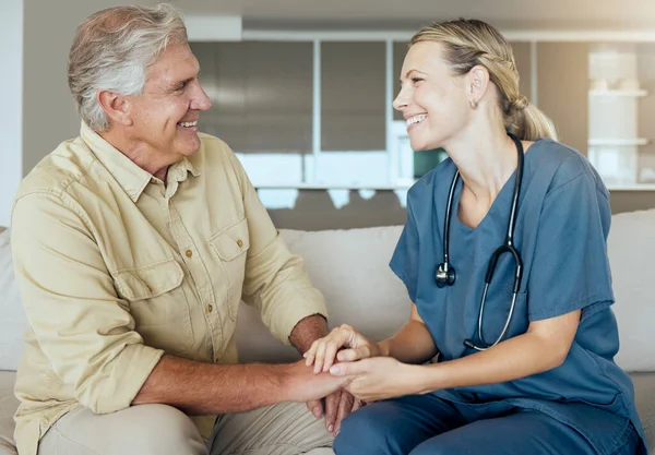 A happy smiling man and woman showing the bond between patient and doctor during a checkup at home. A doctor showing support for her patient while sitting on a sofa chatting and laughing.