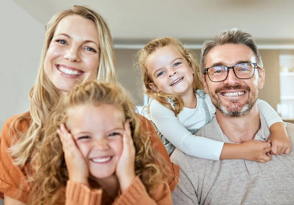 Portrait of a happy Caucasian family of four relaxing in the living room at home. Loving smiling family being affectionate together. Young couple bonding with their little kids at home.