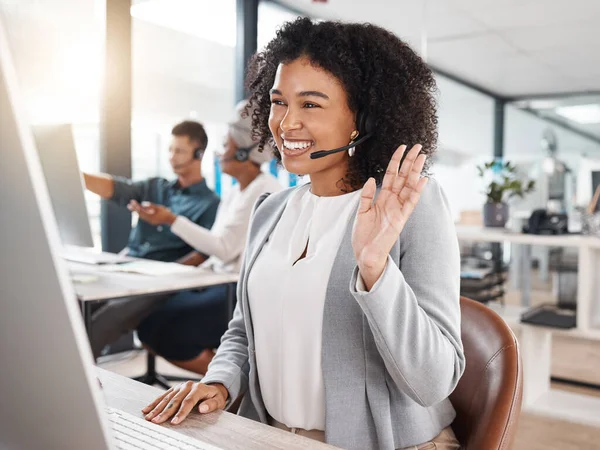 Happy mixed race call centre telemarketing agent waving hello during virtual meeting via video call on a computer in an office. Female consultant greeting client during online discussion for customer