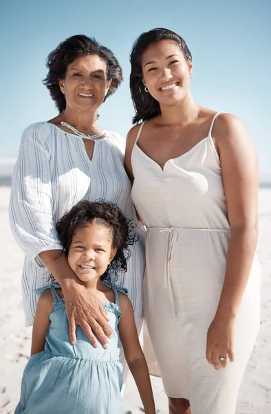 Smiling mixed race family standing together on a beach. Happy hispanic grandmother bonding with granddaughter over a weekend. Adorable little girl enjoying free time with single mother and parent.