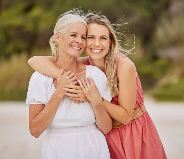 A young caucasian woman spending the day at the beach with her elderly mother. White female and her mother smiling at the beach and hugging each other.
