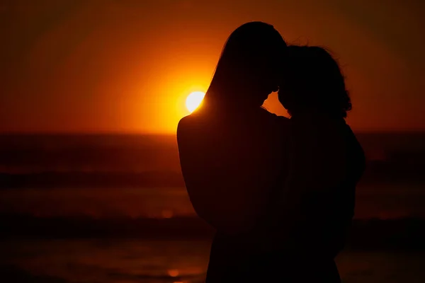 Closeup silhouette of a mother and daughter watching the sunset at the beach . Rear view of of a woman and her little daughter enjoying the ocean view on a day out at the beach.